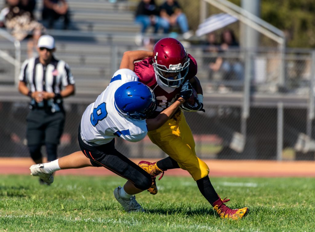 Defensive player number eight has offensive running back with ball wrapped up in his grasp as he attempts to tackle the player during a game